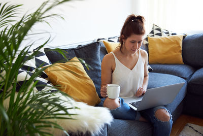 Rear view of woman using mobile phone while sitting on sofa