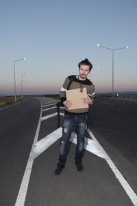 Portrait of man with cardboard standing on road against sky