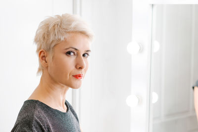 Beautiful woman with short haircut looking in mirror at her home.