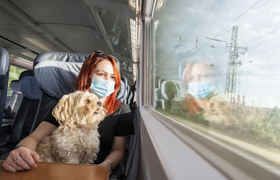 Young woman wearing mask sitting with dog in train