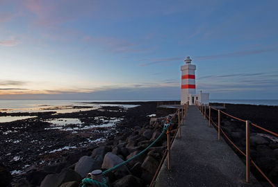Lighthouse by sea against sky during sunset