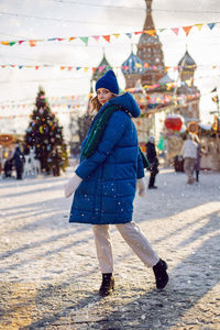 Woman in blue jacket and scarf and white gloves in winter, square in moscow on christmas