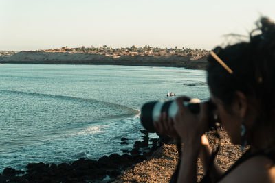 Side view of man photographing sea against clear sky