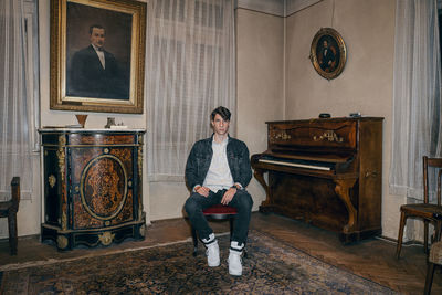 Portrait of young man sitting on chair by piano