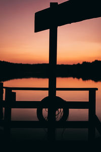 Silhouette man standing by railing against lake during sunset