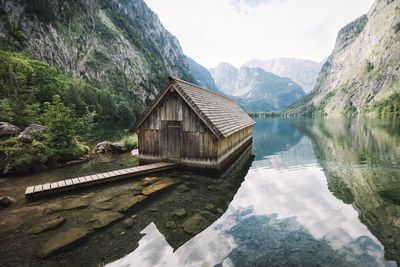 Boathouse in lake by mountains against sky