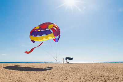 Colorful parachute at beach against sky during sunny day