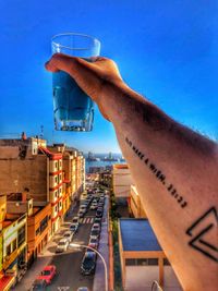 Hand holding glass of cityscape against clear blue sky