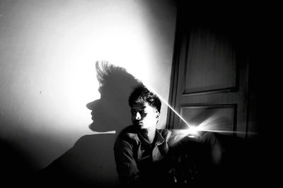 Young man looking away while sitting against wall at home