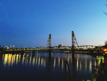 Illuminated bridge over river against blue sky