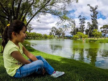 Side view of smiling girl sitting by lake at park