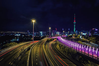 Light trails on road amidst buildings against sky at night