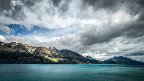 Scenic view of sea by mountain against sky