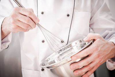 Midsection of chef holding wire whisk and bowl