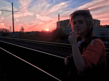Portrait of young woman standing on railroad track during sunset