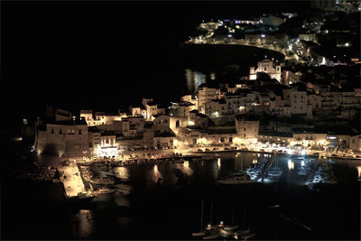 High angle view of illuminated buildings by sea against sky at night