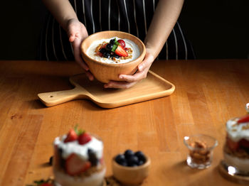 Midsection of woman holding ice cream in bowl on table