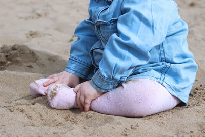 Low section of baby sitting on sand at beach