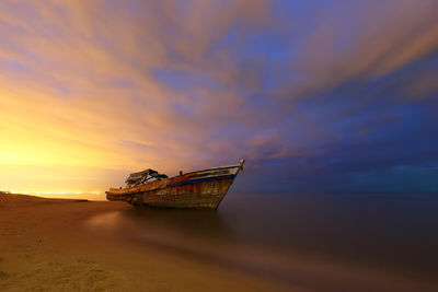 Boat moored on sea against cloudy sky at sunset