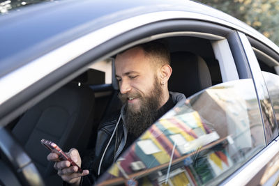 Bearded man using mobile phone while sitting in car seen through window