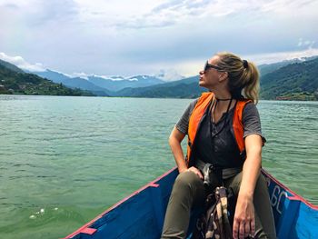 Female hiker wearing sunglasses traveling in boat on lake against sky
