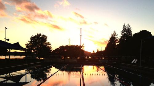 Reflection of silhouette trees in calm lake during sunset