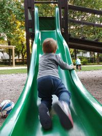 Rear view of boys playing on slide at playground