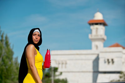 Side view of woman in hijab holding bottle outdoors