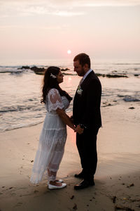 Friends standing on beach against sky during sunset