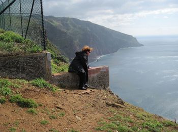 Woman sitting on retaining wall while looking at sea from ponta do pargo