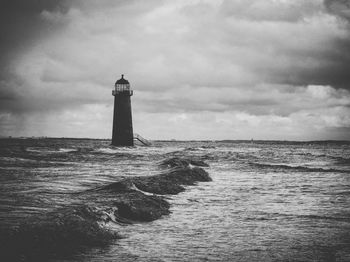 Lighthouse on beach against cloudy sky