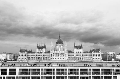 Hungarian parliament building in city against cloudy sky