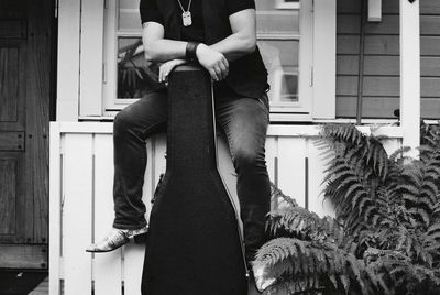 Rear view of man holding guitar case standing in front of building