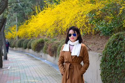 Portrait of fashionable woman standing on footpath against plants