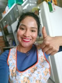 Portrait of smiling young woman showing thumbs up at home