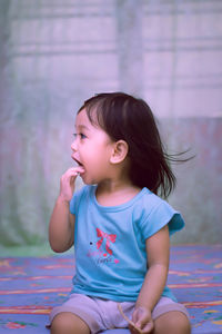 Close-up of cute girl sitting against wall