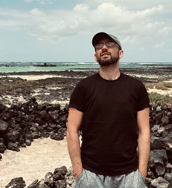 Portrait of young man standing at beach against sky