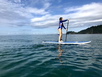 Full length of girl paddleboarding in sea against cloudy sky
