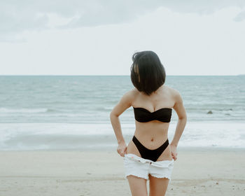 Rear view of young woman healthy body standing on beach wearing black bikini 