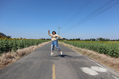 Happy woman jumping on road against clear blue sky