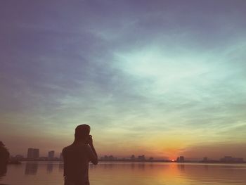 Rear view of man photographing lake against sky during sunset