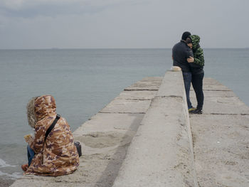 Rear view of man standing on retaining wall against sea