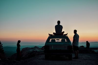 People standing by sea against sky during sunset