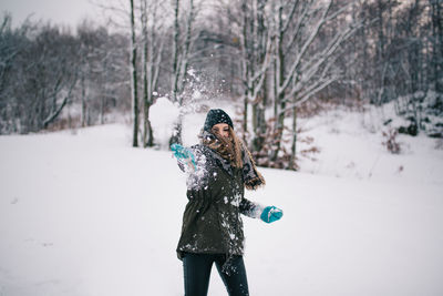 Woman throwing snow against bare trees