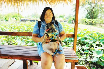 Portrait of woman sitting with dog on bench at park