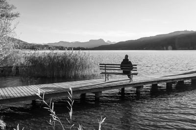 Rear view of man on pier over lake against sky