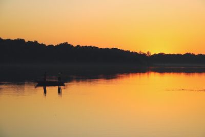 Silhouette men in lake against sky during sunset