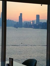 Sea by buildings against sky during sunset