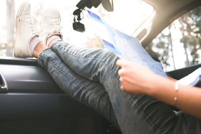 Low section of woman legs on dashboard while holding map in car