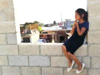 Side view of young woman sitting on wall